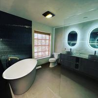 Luxurious modern bathroom featuring sleek large-format tile flooring, a freestanding bathtub with a gold faucet, and dual oval LED mirrors above a floating vanity.