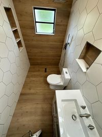 Minimalist Bathroom with Wood and Hexagonal Tile Design: A sleek bathroom featuring a wood-paneled ceiling and floor, white hexagonal wall tiles, and built-in shelving for a streamlined, natural design.