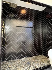 Bold Black Herringbone Shower with Pebble Flooring: A striking shower design with black herringbone tiles, a recessed niche, and pebble flooring for a unique and dramatic look.